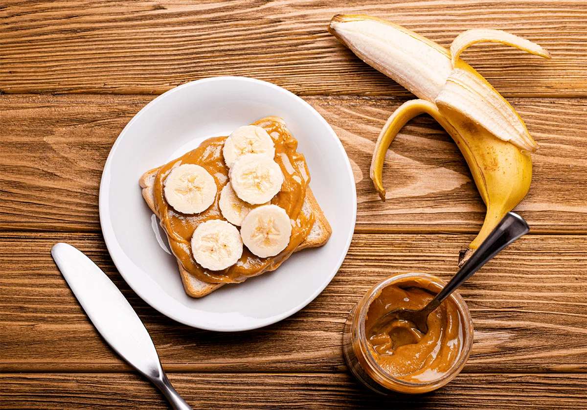 A slice of toast with peanut butter and banana slices on a white plate, next to a peeled banana and a jar of peanut butter—just the kind of simple, nourishing breakfast enjoyed at MorningStar Senior Living Hillsboro's retirement living community.