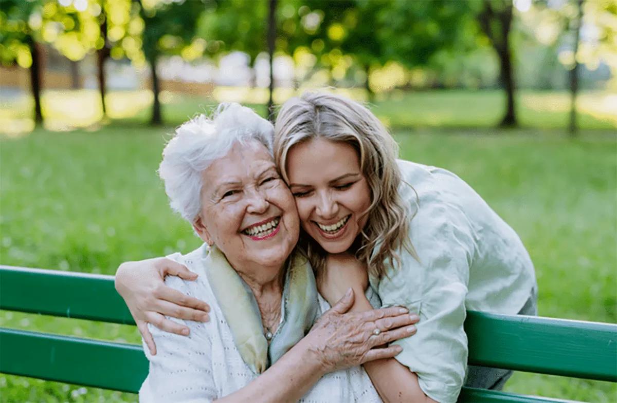 Moving-2 A senior woman sitting on a bench being hugged by a younger woman.