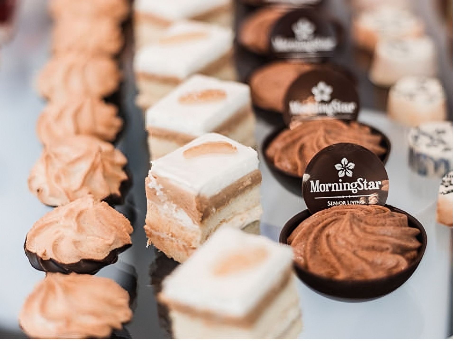 An assortment of elegant desserts, including layered cakes, meringue cookies, and chocolate cups labeled
