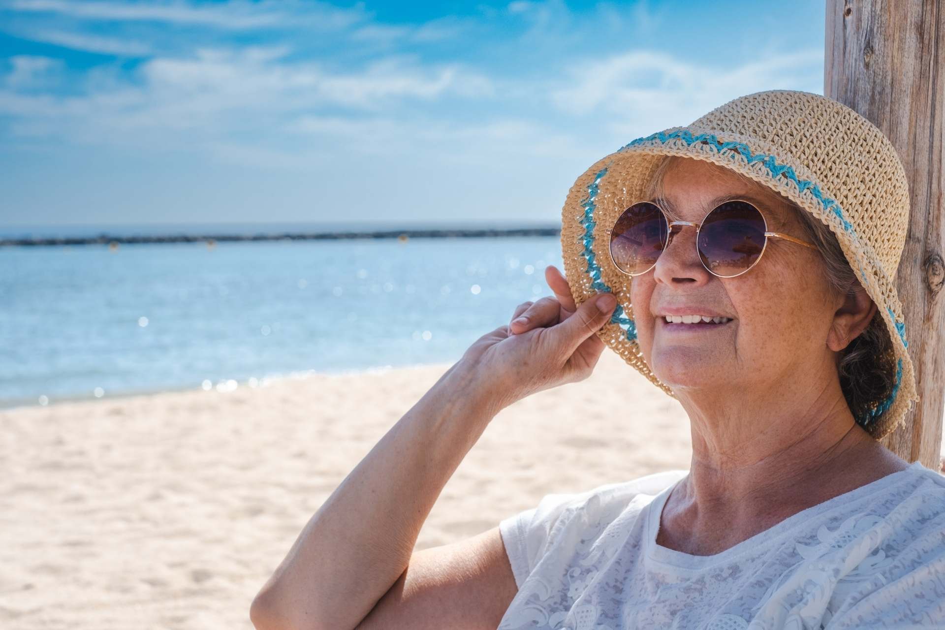 smiling-senior-woman-with-summer-hat-and-sunglasses A senior woman enjoying a beach day in the shade.